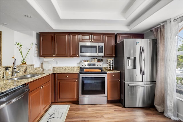 kitchen with light wood finished floors, a raised ceiling, light stone counters, appliances with stainless steel finishes, and a sink