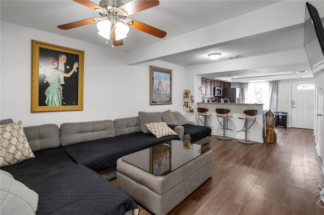 living room featuring a textured ceiling, dark wood-type flooring, and ceiling fan