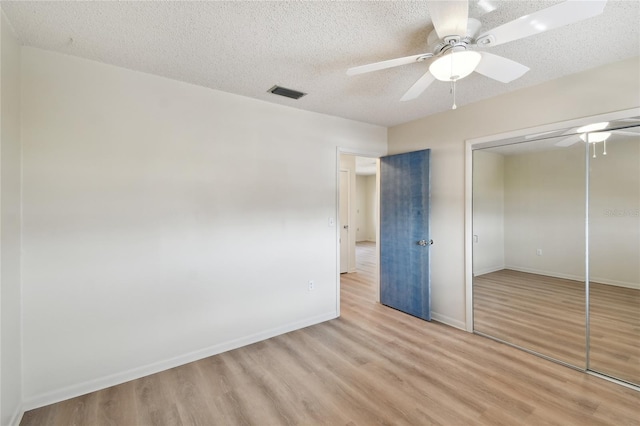 unfurnished bedroom featuring ceiling fan, a textured ceiling, a closet, and light wood-type flooring