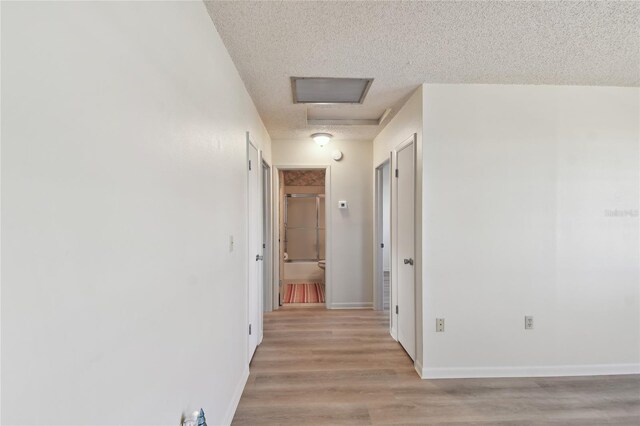 hall with light wood-type flooring and a textured ceiling