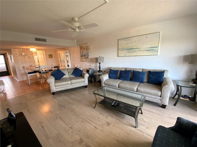 living room featuring light hardwood / wood-style floors, a textured ceiling, and ceiling fan