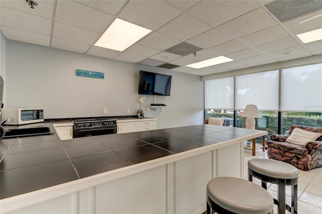 kitchen with a paneled ceiling, white cabinetry, kitchen peninsula, black range, and tile countertops