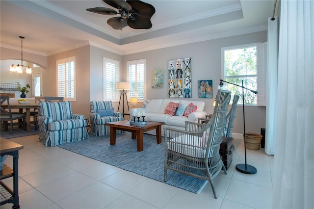 tiled living room featuring a raised ceiling, ornamental molding, and ceiling fan with notable chandelier