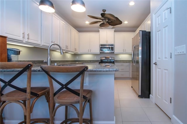 kitchen with appliances with stainless steel finishes, a breakfast bar, white cabinetry, dark stone countertops, and crown molding