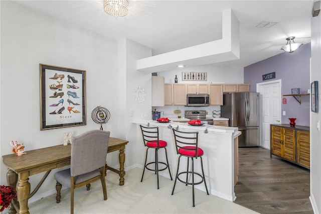 kitchen featuring appliances with stainless steel finishes, a kitchen bar, light brown cabinets, wood-type flooring, and kitchen peninsula