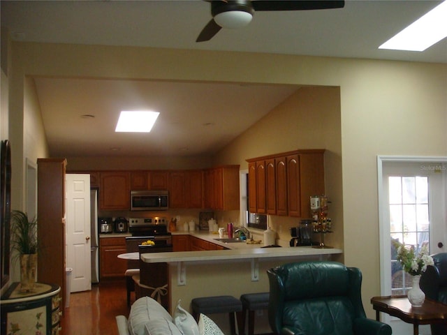 kitchen with sink, appliances with stainless steel finishes, vaulted ceiling with skylight, a kitchen bar, and kitchen peninsula