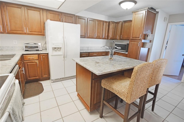 kitchen featuring light tile patterned flooring, a kitchen island, a kitchen breakfast bar, white fridge with ice dispenser, and light stone counters