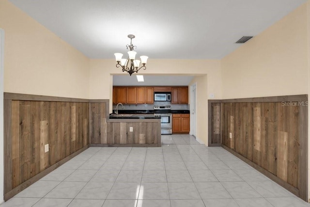 kitchen featuring appliances with stainless steel finishes, pendant lighting, wooden walls, a notable chandelier, and kitchen peninsula