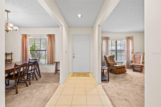 entrance foyer with light colored carpet, a wealth of natural light, a chandelier, and a textured ceiling