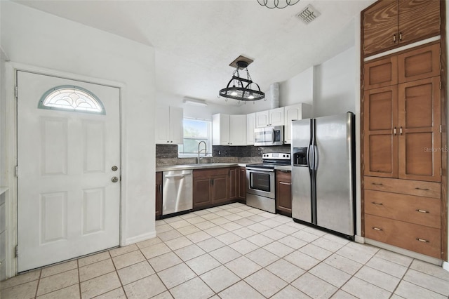 kitchen featuring pendant lighting, sink, backsplash, white cabinetry, and stainless steel appliances