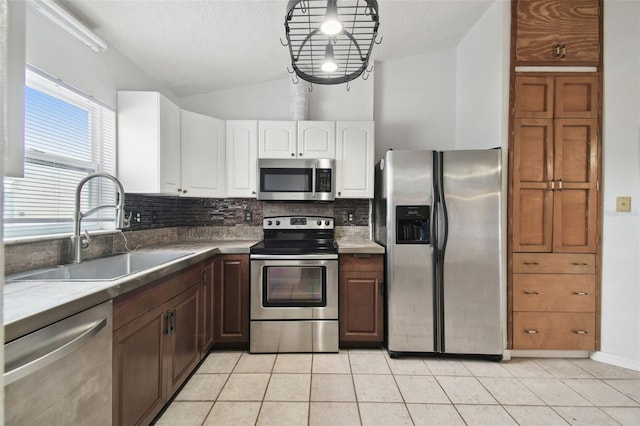 kitchen with lofted ceiling, white cabinetry, stainless steel appliances, sink, and light tile patterned floors