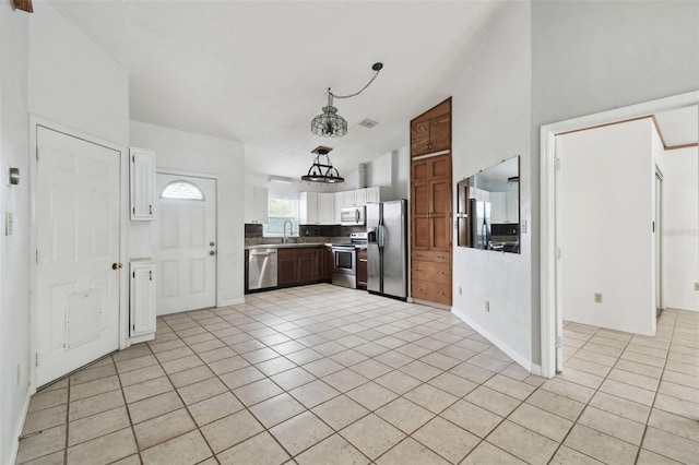 kitchen with vaulted ceiling, light tile patterned floors, decorative backsplash, white cabinets, and stainless steel appliances