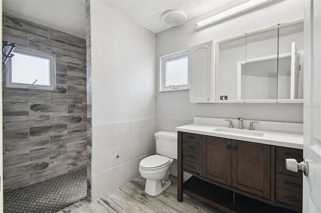 bathroom featuring toilet, a textured ceiling, wood-type flooring, tiled shower, and vanity