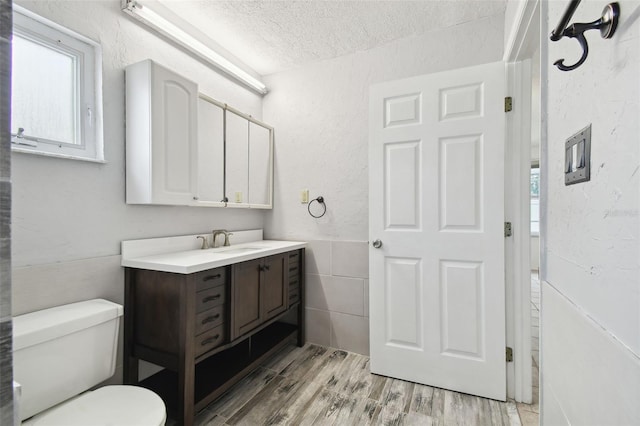 bathroom with wood-type flooring, tile walls, toilet, a textured ceiling, and vanity