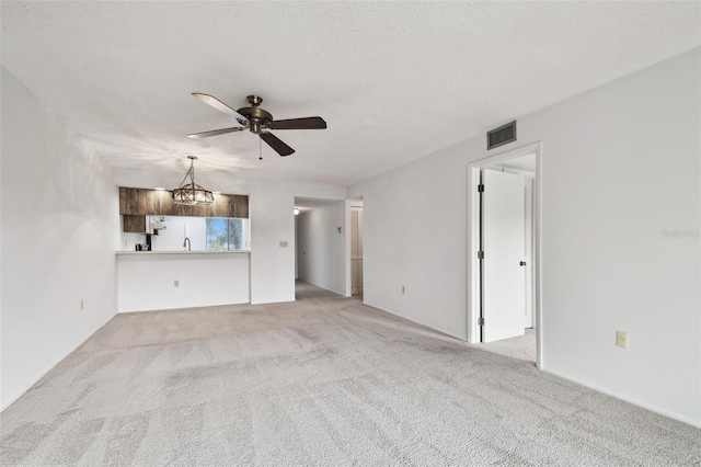 unfurnished living room featuring ceiling fan with notable chandelier, light carpet, and a textured ceiling