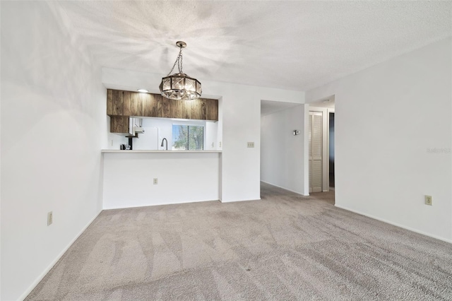 unfurnished living room featuring carpet floors, sink, a textured ceiling, and a chandelier