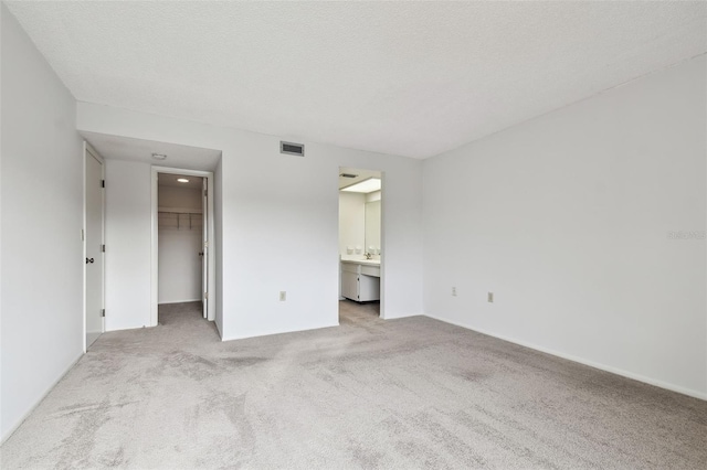 unfurnished bedroom with connected bathroom, a spacious closet, a textured ceiling, a closet, and light colored carpet