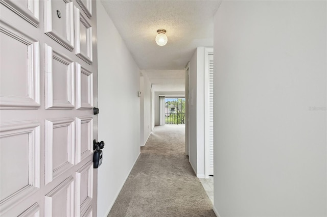 hallway with light colored carpet and a textured ceiling