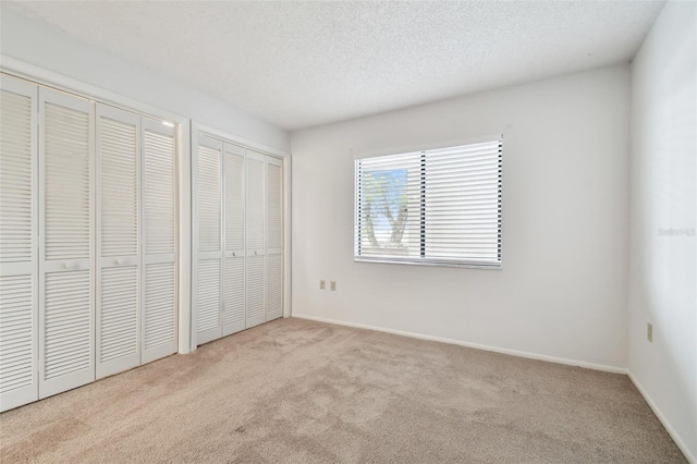 unfurnished bedroom featuring a textured ceiling, light colored carpet, and multiple closets