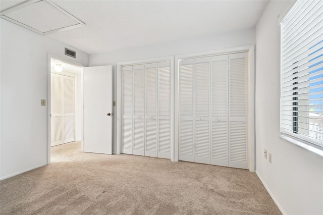 unfurnished bedroom featuring light carpet and two closets