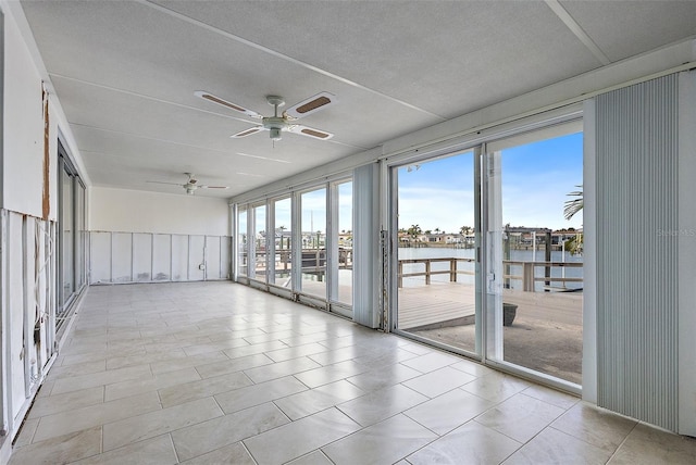 unfurnished sunroom featuring ceiling fan and a water view