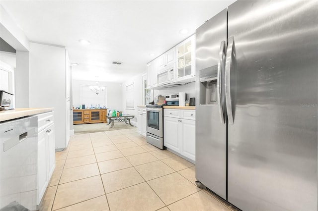 kitchen with white cabinets, appliances with stainless steel finishes, light tile patterned flooring, and a notable chandelier