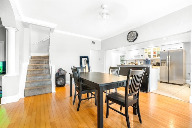 dining room with light hardwood / wood-style floors, crown molding, and ornate columns