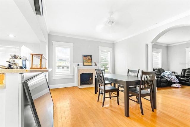 dining space with ceiling fan, decorative columns, ornamental molding, and light wood-type flooring