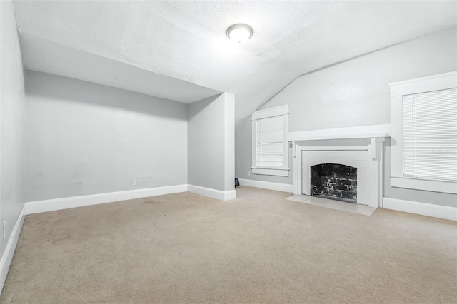 unfurnished living room featuring a textured ceiling, lofted ceiling, and light colored carpet