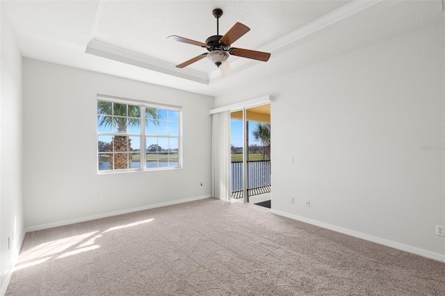 carpeted spare room featuring crown molding, a raised ceiling, ceiling fan, and a water view