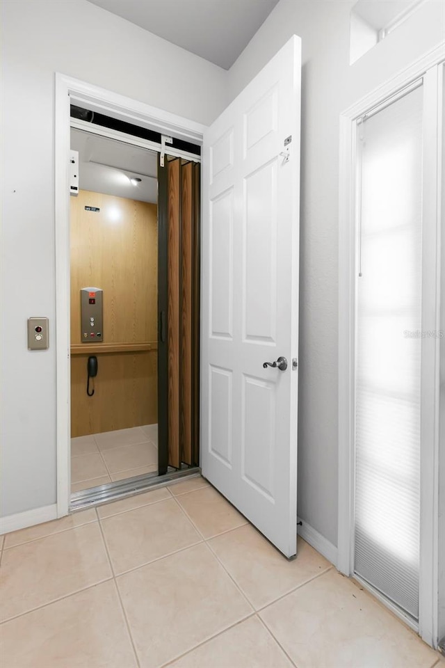 corridor featuring elevator and light tile patterned floors