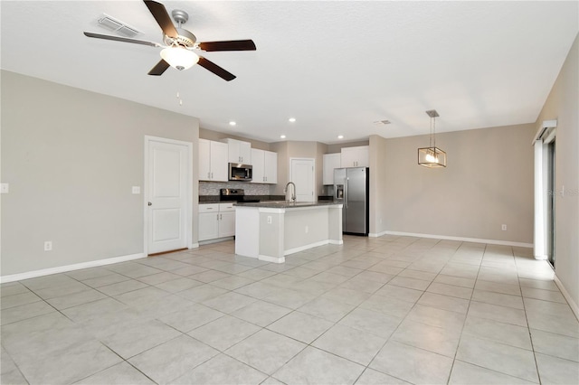 kitchen with tasteful backsplash, hanging light fixtures, a center island with sink, appliances with stainless steel finishes, and white cabinets