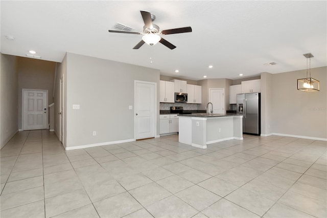 kitchen featuring stainless steel appliances, white cabinets, hanging light fixtures, dark countertops, and a center island with sink