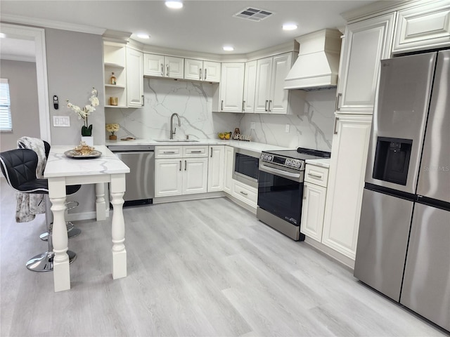 kitchen featuring sink, light wood-type flooring, appliances with stainless steel finishes, custom range hood, and backsplash