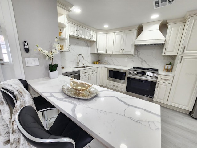 kitchen featuring light stone counters, visible vents, premium range hood, a sink, and stainless steel appliances