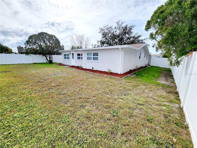 rear view of property featuring a fenced backyard, a lawn, and stucco siding