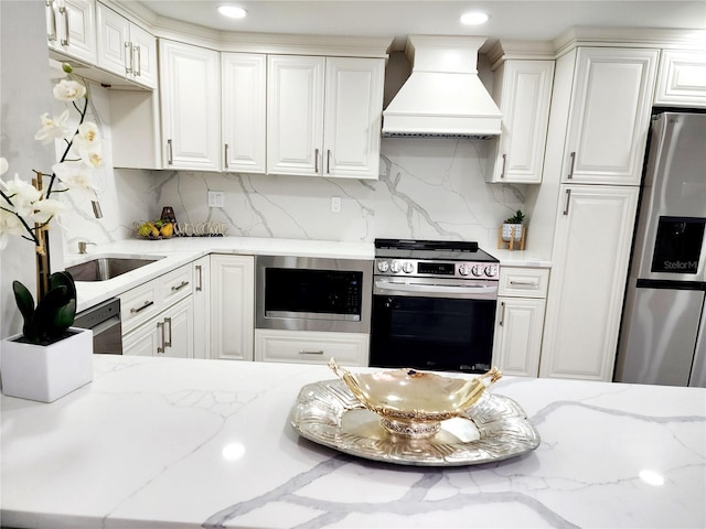 kitchen featuring white cabinetry, stainless steel appliances, custom range hood, and a sink