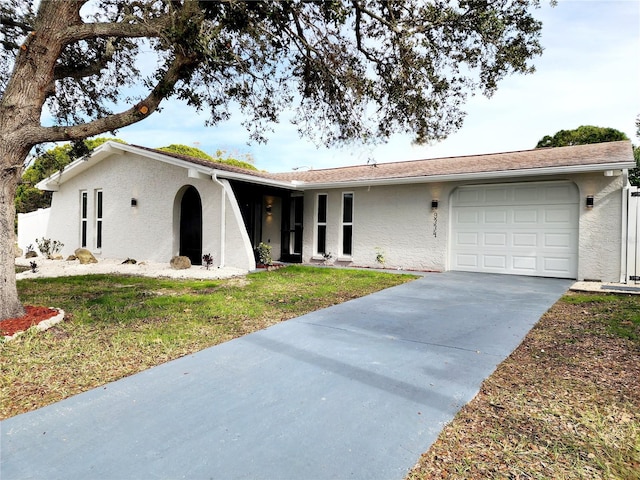 ranch-style home featuring concrete driveway, an attached garage, a front lawn, and stucco siding