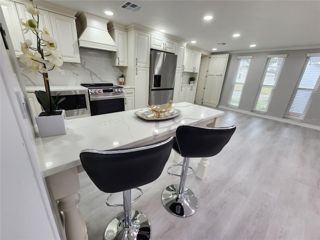 kitchen featuring visible vents, light wood-style flooring, backsplash, appliances with stainless steel finishes, and custom exhaust hood