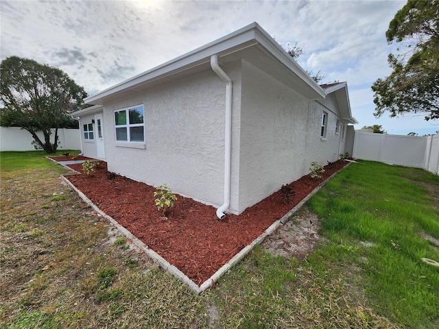 view of side of property featuring stucco siding, a lawn, and a fenced backyard