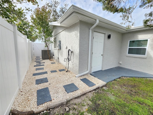 property entrance featuring stucco siding, a patio, central AC unit, and fence