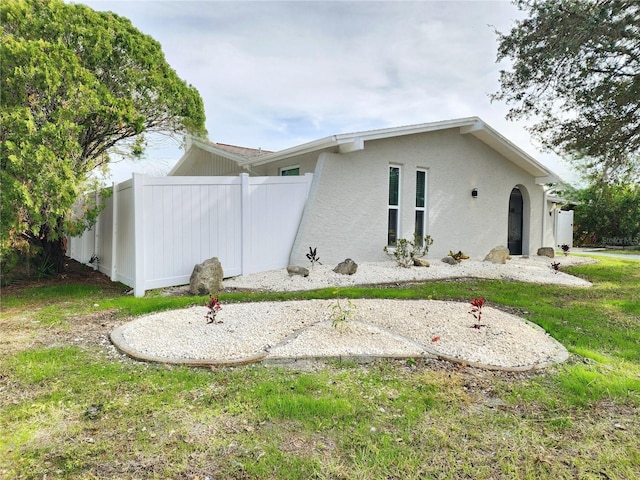 view of side of property featuring stucco siding, a lawn, and fence