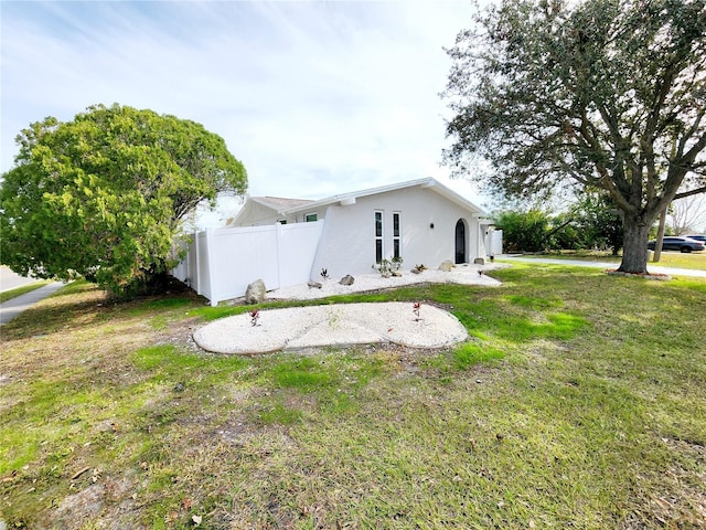 view of side of home with stucco siding, a lawn, and fence