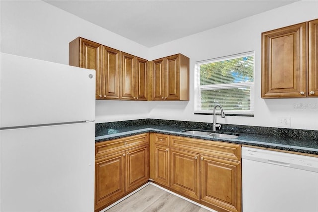 kitchen with sink, white appliances, light hardwood / wood-style flooring, and dark stone countertops