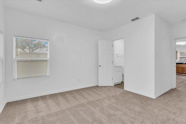 unfurnished bedroom featuring light carpet and connected bathroom