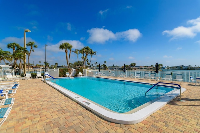 pool with a water view, fence, and a patio