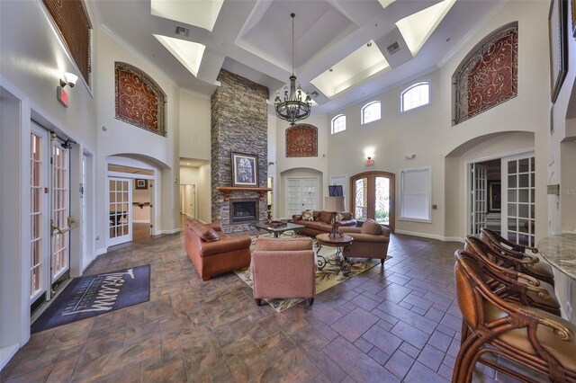 living room featuring a high ceiling, an inviting chandelier, french doors, and a stone fireplace