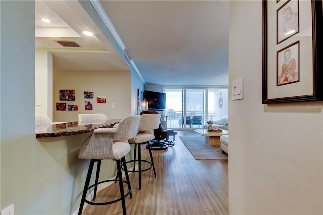 kitchen featuring ornamental molding, light hardwood / wood-style floors, floor to ceiling windows, and a breakfast bar