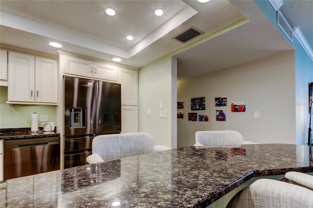 kitchen featuring white cabinetry, stainless steel dishwasher, a raised ceiling, fridge with ice dispenser, and a breakfast bar area