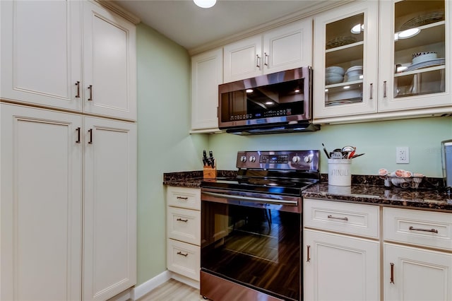 kitchen with light hardwood / wood-style floors, dark stone counters, white cabinetry, and appliances with stainless steel finishes